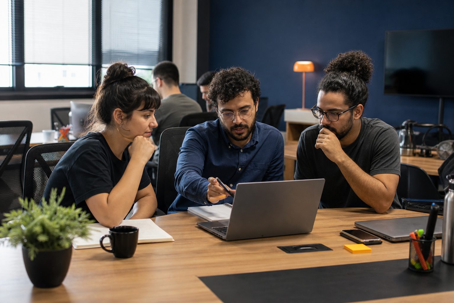 Equipe de tecnologia colabora em torno de um notebook em um escritório.